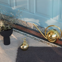"Gold watering can and decorative vase on a striped rug with earthy and neutral tones."
