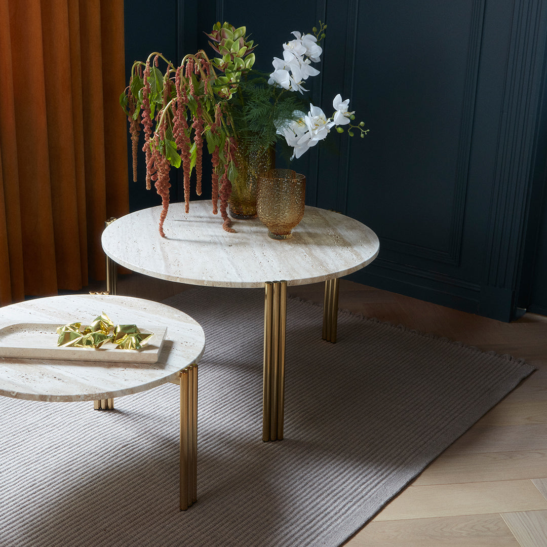 Marble-patterned coffee tables with gold legs, set on a textured beige rug, accentuated by vibrant green and white flowers.