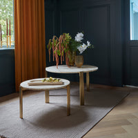 Marble-top coffee tables with gold legs, set against a dark blue wall and warm orange curtains, featuring a neutral patterned rug.