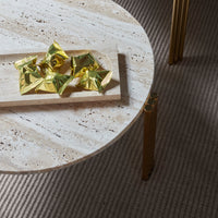Golden foil decorations on a round beige marble table with a textured cream rug underneath.