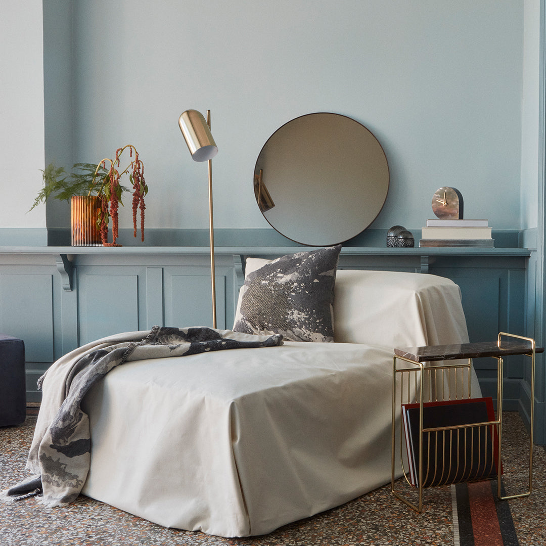 Cozy beige chair cover with a stylish gray throw and patterned pillow, against a soft blue wall backdrop.