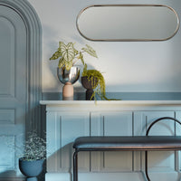 Stylish blue wall with oval mirror, black and metallic vases, and green plants adding vibrant contrast.