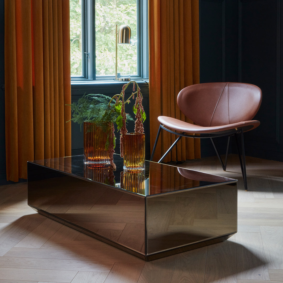 "Stylish coffee table with a sleek black finish, surrounded by vibrant orange curtains and a warm brown chair."