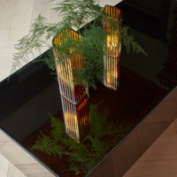 Amber and black geometric vases with vertical stripes, set against a dark tabletop and lush green foliage.