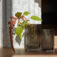 "Clear glass vases with ribbed patterns, featuring green leaves and pink accents against a speckled white backdrop."