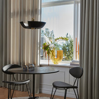 Modern black pendant light with neutral curtains, round table, and a vibrant yellow vase with greenery. Elegant and stylish decor.