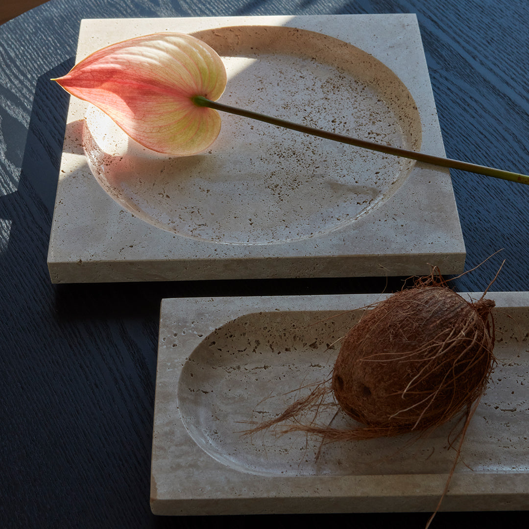 Beige and cream textured serving trays with smooth surfaces, accented by a soft pink flower and natural elements.