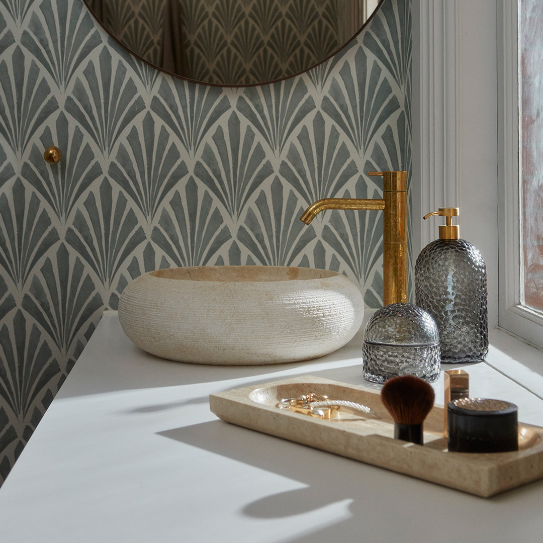 Elegant green and gray art deco pattern wallpaper with golden accents and textured accessories in a modern bathroom setting.
