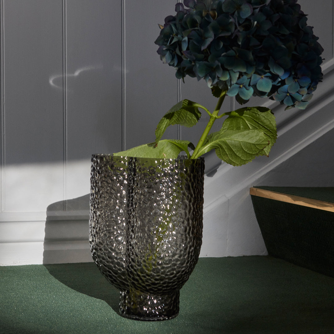 Black textured vase with a shiny finish, featuring a hammered pattern, showcasing blue hydrangea flowers.