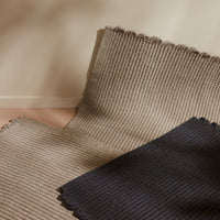 Stack of textured rugs in beige and navy blue with subtle ribbed patterns and fringed edges. Perfect for modern decor.