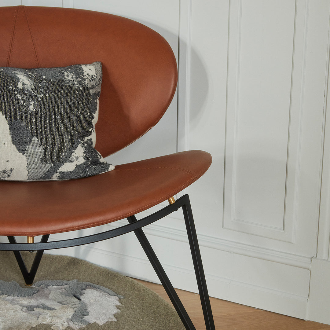 Brown leather chair with a black metal frame and a gray and white patterned pillow. Soft textures and modern design.