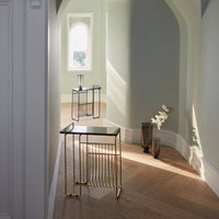 Modern gold and black side tables against soft green walls and warm wood floors with elegant light reflections.