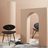 Black chairs with minimalist design, set against soft peach background and geometric cream arch, on a patterned rug.