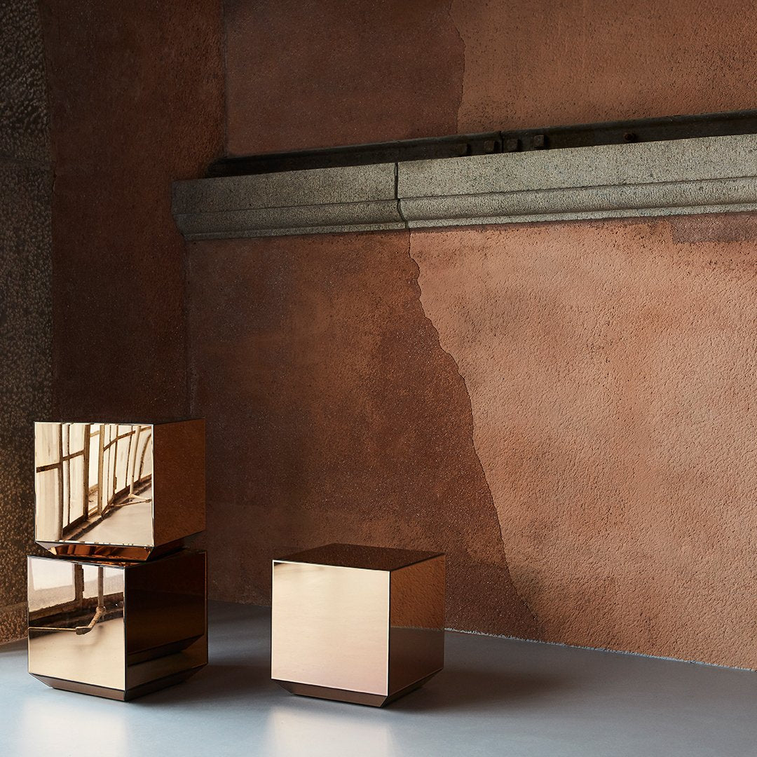 Copper mirror finish cubes against a textured warm-toned wall, featuring sleek geometric shapes and reflective surfaces.
