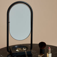 Black metal mirror with an oval shape on a sleek marble surface, complemented by gold and rosy accents.