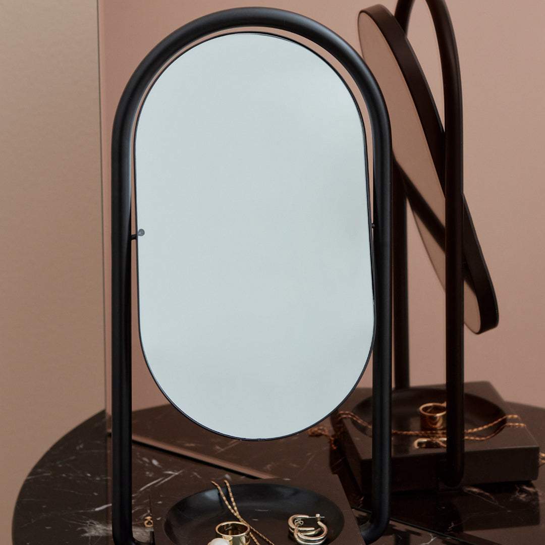 Black arc-shaped mirror with a smooth reflective surface, set against a minimalist backdrop.