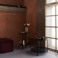 "Elegant black metal side tables against a warm terracotta wall, with rich burgundy accents and soft neutral flooring."