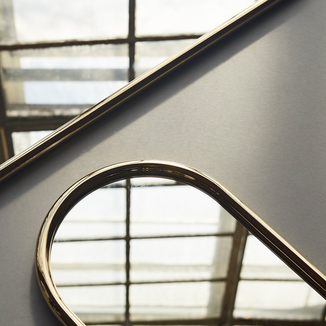 Gold-trimmed mirror on a sleek gray background, reflecting light through a geometric window pattern.