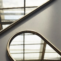 Gold-trimmed mirror on a sleek gray background, reflecting light through a geometric window pattern.