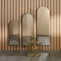 Three arched mirrors with a warm gold finish against a textured beige wall, complemented by a modern, clear acrylic table.