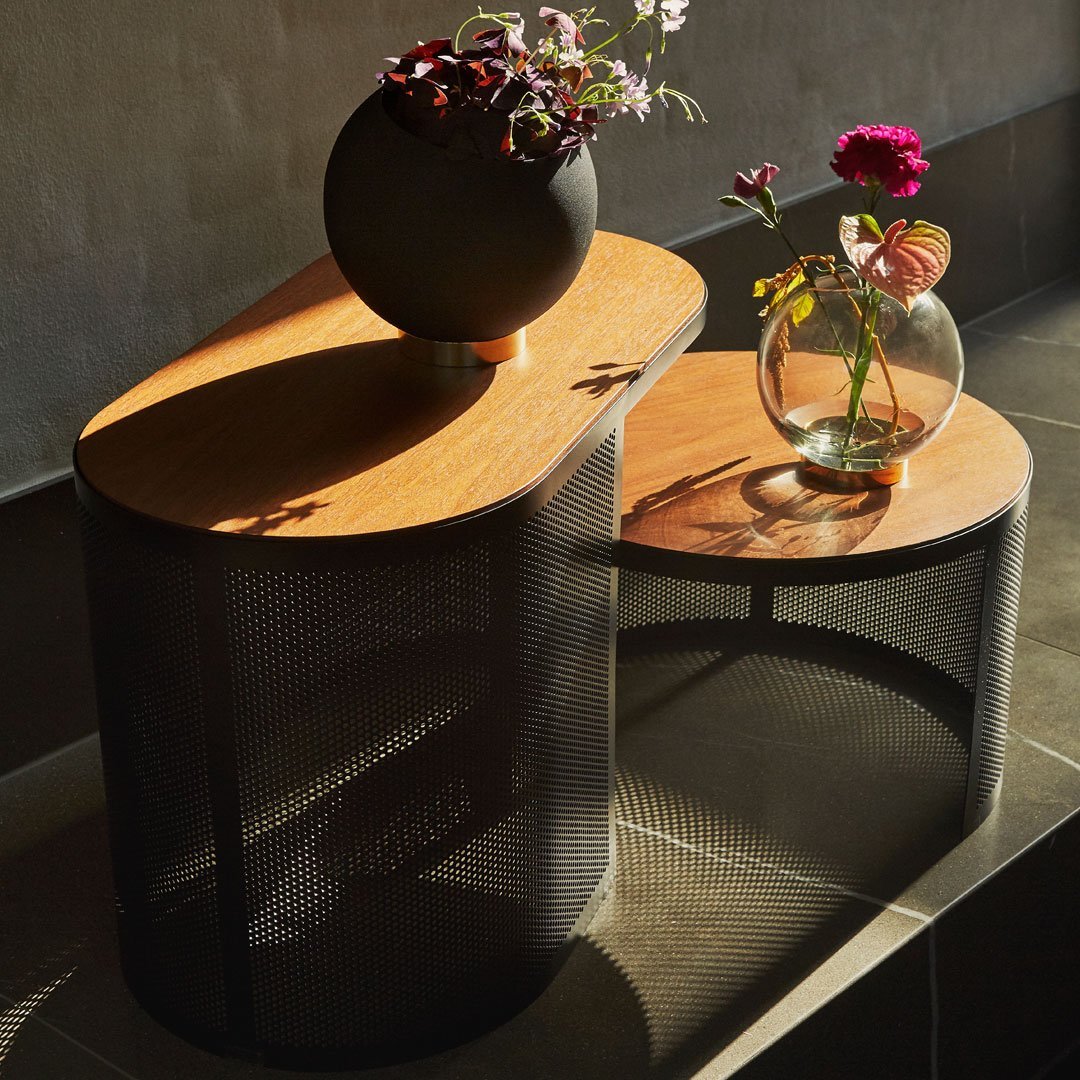 Modern two-tone coffee table with an oak top and black mesh base, featuring elegant floral arrangements.
