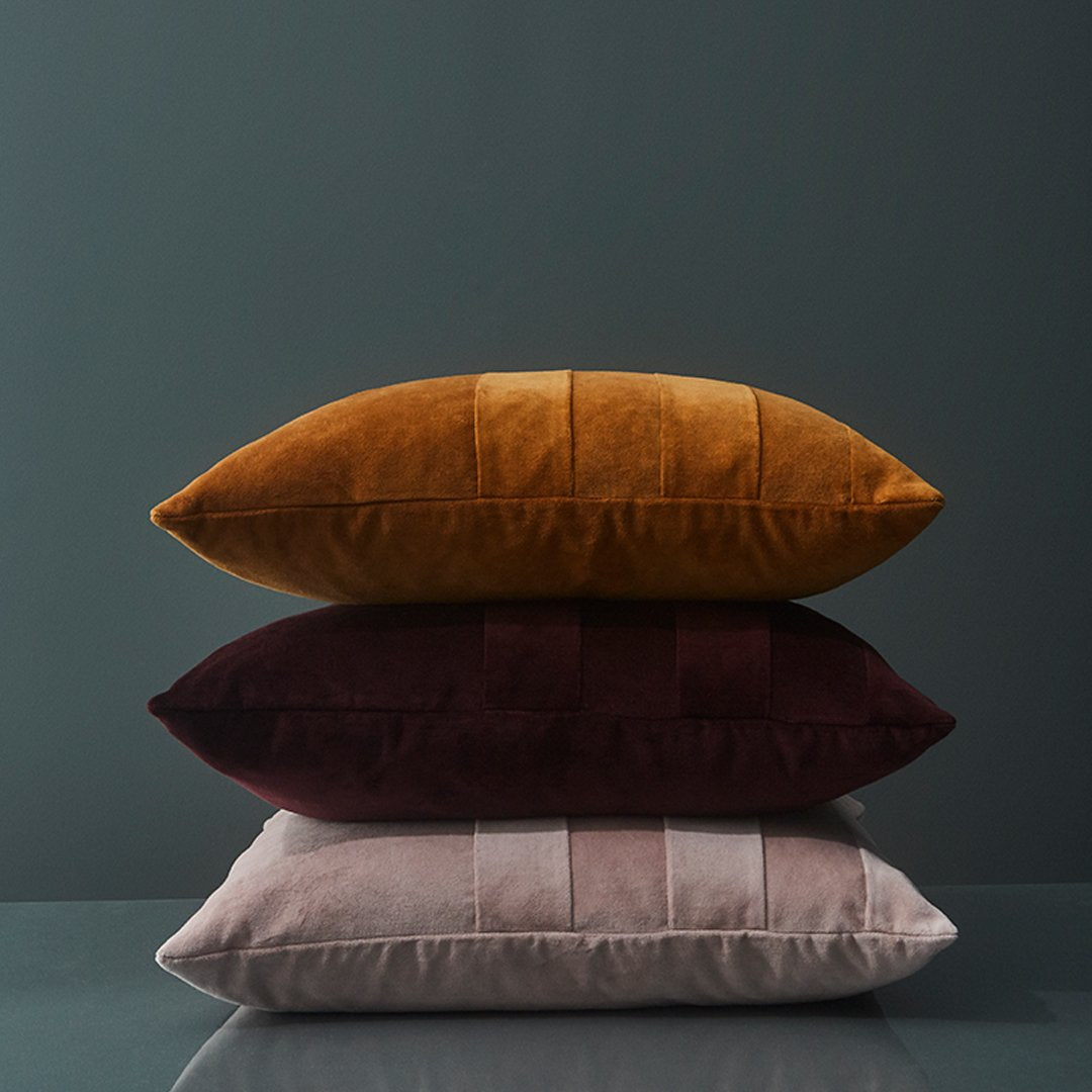 Decorative pillows in mustard, deep burgundy, and soft pink with textured stripes, stacked on a sleek surface.
