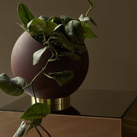 Brown round planter with gold base, featuring lush green trailing leaves. Elegant and modern design for home decor.