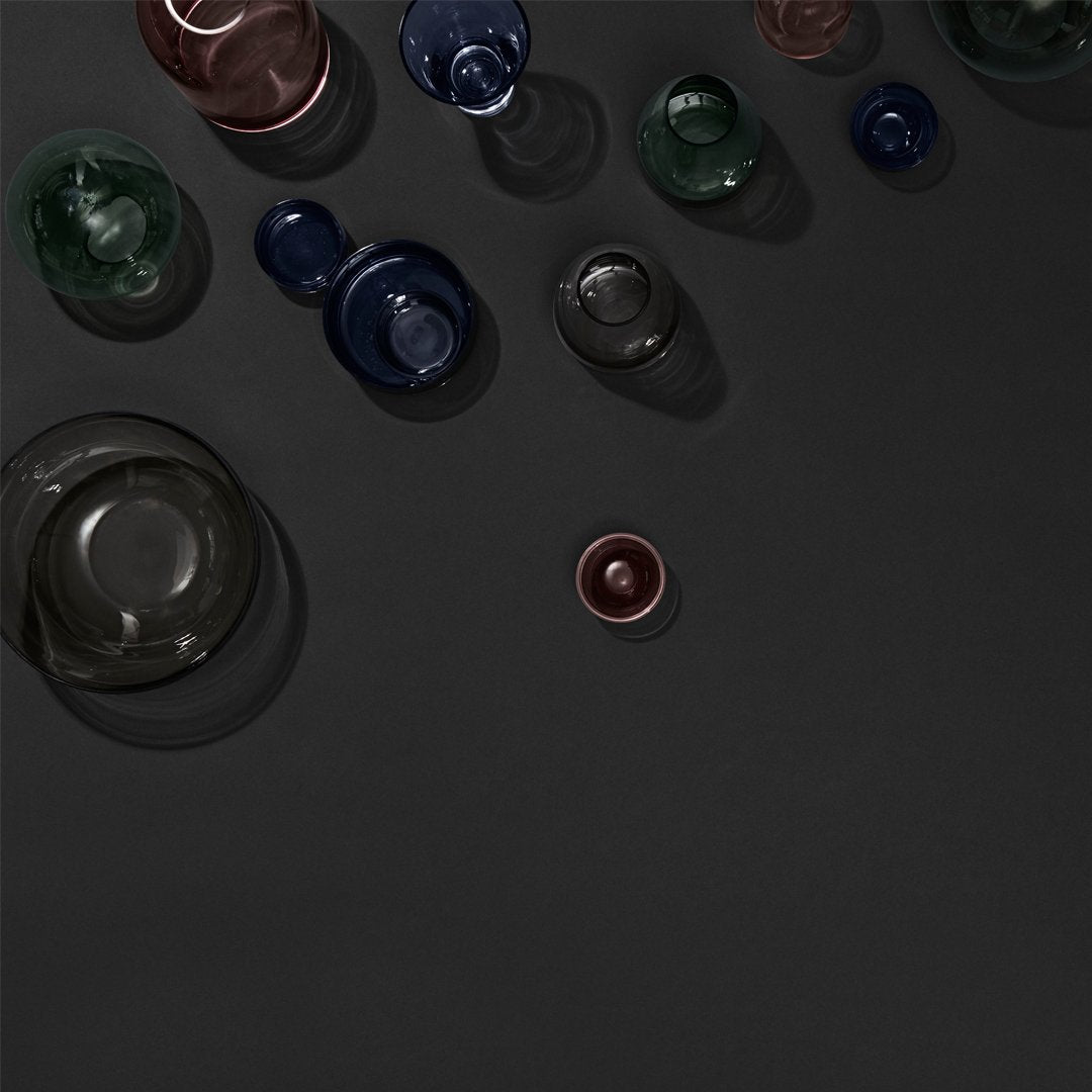 "Colorful glass bowls in green, blue, dark red, and clear, arranged on a sleek black background."