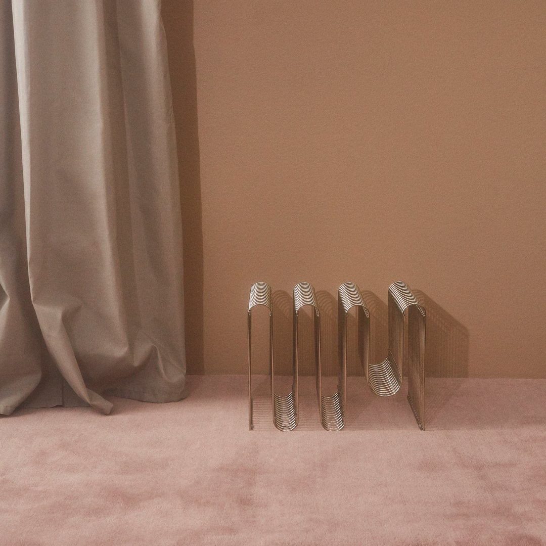 Metal bookends in a sleek silver finish against a soft pink backdrop and neutral beige curtain.