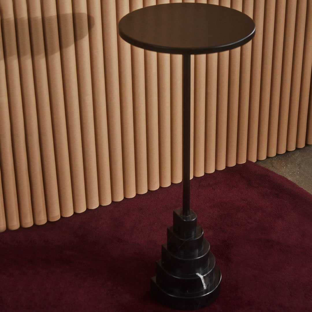 "Black side table with a spiral base, set against warm wood and deep burgundy background."