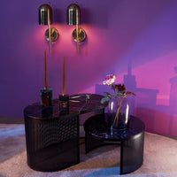 Black geometric side table with marble top, accented by gold sconces against a vibrant purple wall.