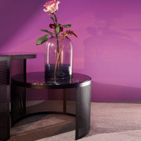 Black round table with textured pattern, featuring a clear vase and a pink rose against a vibrant purple wall.
