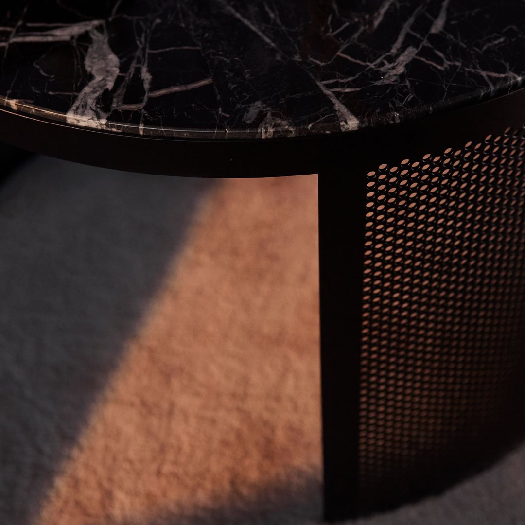 Black marble tabletop with white veining and a textured black metal mesh side panel. Warm light casts soft shadows.