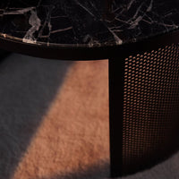 Black marble tabletop with white veining and a textured black metal mesh side panel. Warm light casts soft shadows.