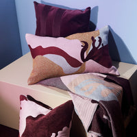 "Textured pillows in burgundy, pink, and cream with abstract patterns on a cream surface."