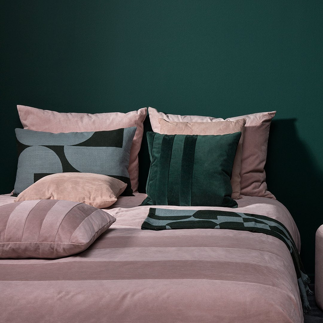 "Pink striped bedding with green and gray patterned pillows against a dark green background."