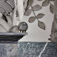 Elegant gray glass orb on a textured marble shelf, featuring intricate leaf patterns and green marble accents.