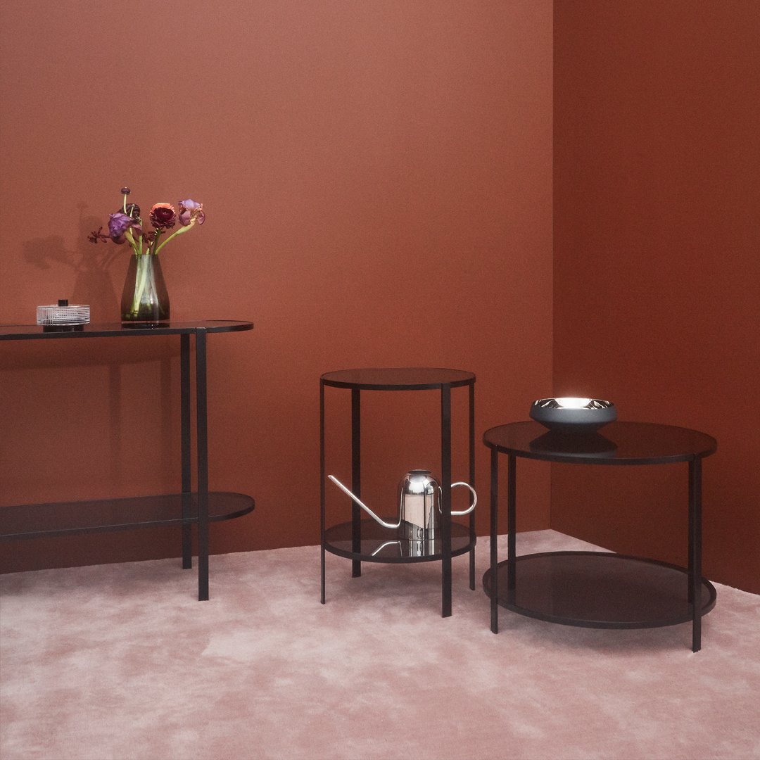 "Modern furniture set with black metal frames, deep brown tabletops, and a warm terracotta wall backdrop."