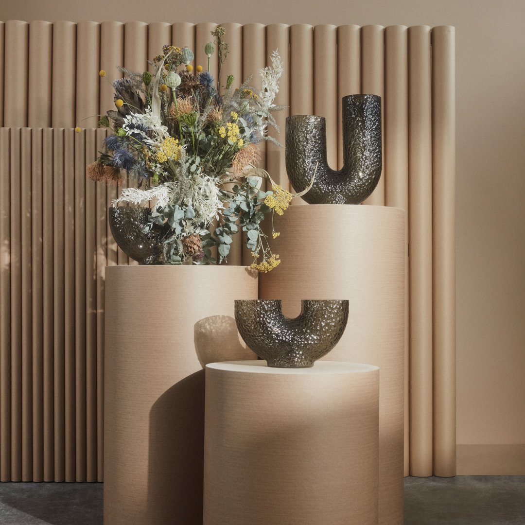 "Textured black vases with earthy tones and floral arrangements, set against warm beige and soft pastel backgrounds."