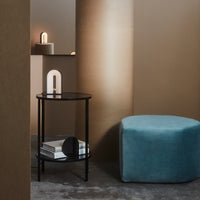 Modern interior featuring a black metal side table and a soft blue ottoman against warm brown walls.