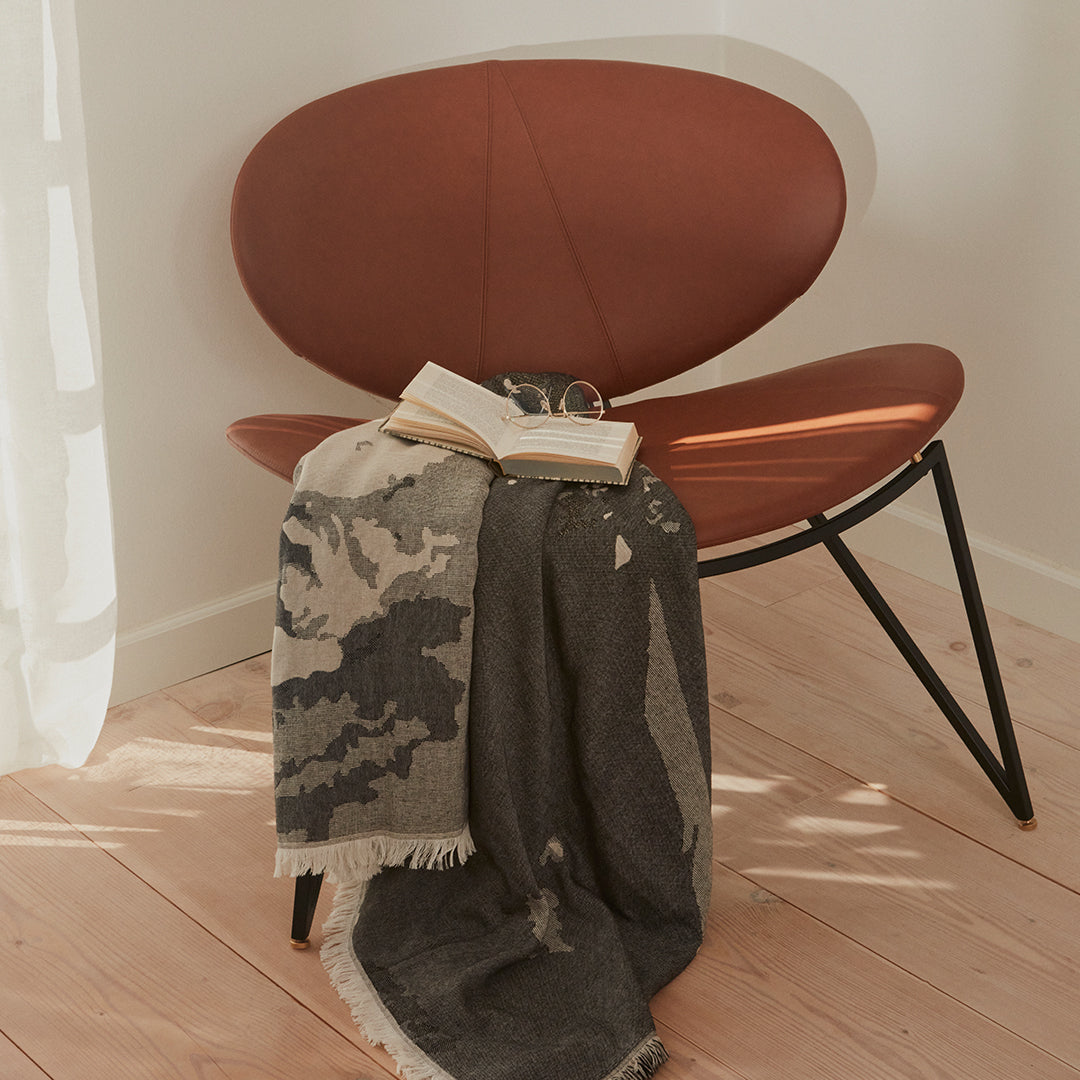 Gray and beige patterned blanket draped over a stylish chair, creating a cozy and modern home aesthetic.