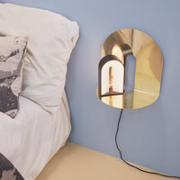 Gold wall lamp with curved shapes, reflecting light against a soft blue wall, complemented by textured white bedding.