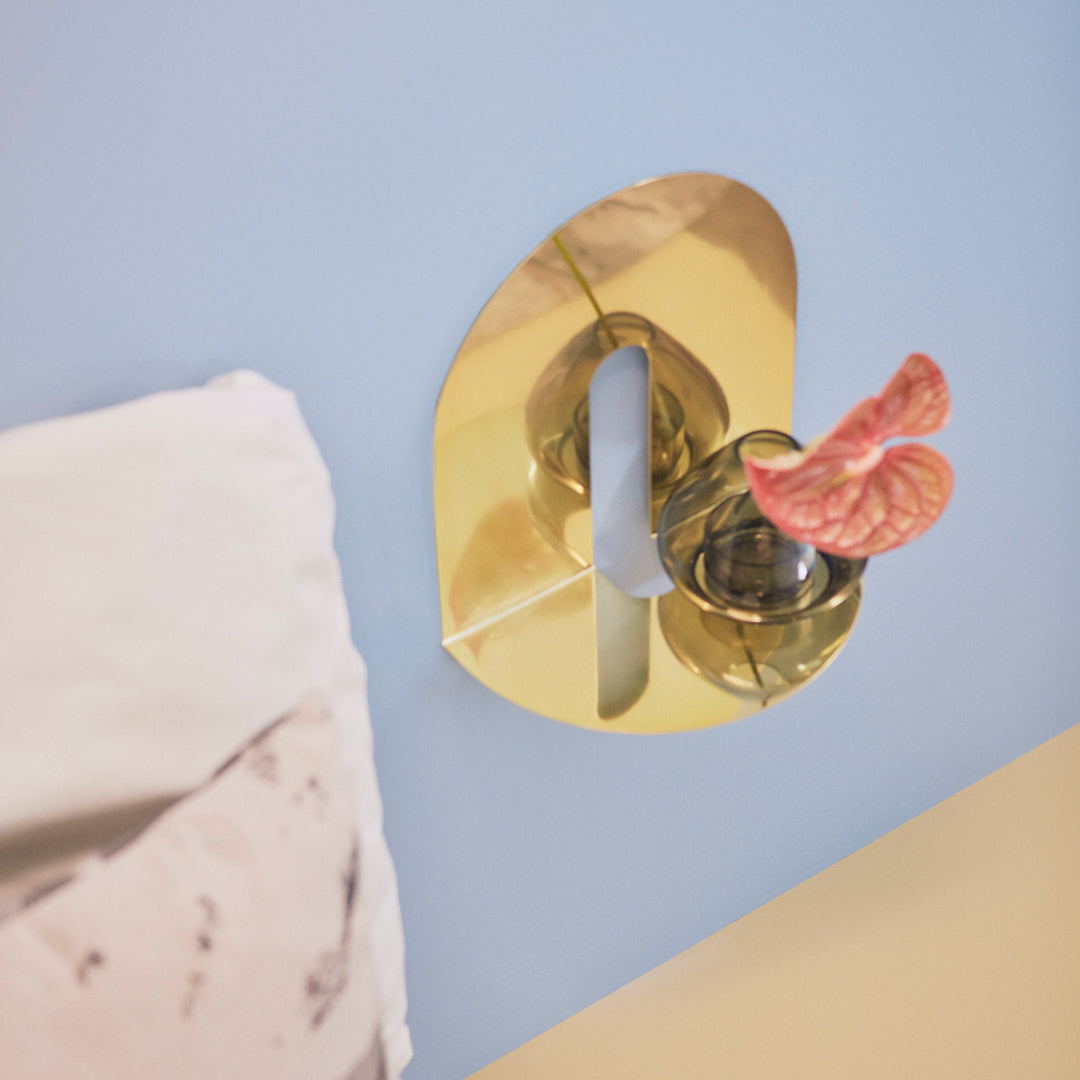Gold abstract wall hook with a pink decorative accent, set against a light blue and cream background.