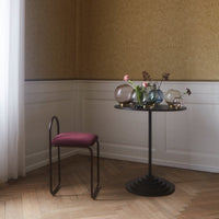 Modern black table with a round top, featuring a deep burgundy chair, set against a textured gold wallpaper backdrop.