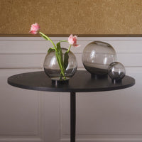 Clear glass vases in various sizes on a sleek black table with pink tulips, set against a warm, patterned background.