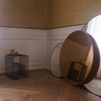 Stylish black and bronze geometric tables with round mirrors, set against a warm, textured wall and wooden floor.