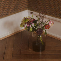 "Vibrant floral arrangement in a glass vase with purple, pink, and green hues against a textured wall pattern."