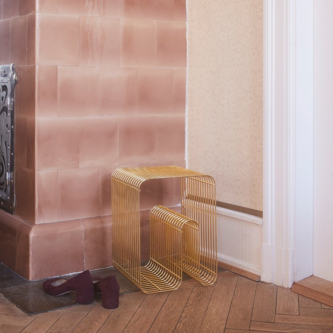 Gold wireframe side table beside a pink wall, featuring clean lines and geometric patterns.