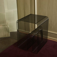 Black wireframe side table with an open design, featured on a burgundy carpet against a neutral wall.