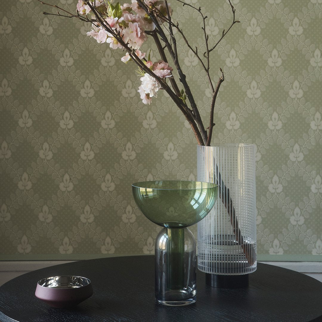 Green and clear glass vases on a black table, against a textured sage green patterned wall.
